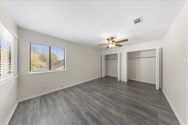 an empty room with wooden floor chandelier fan and windows