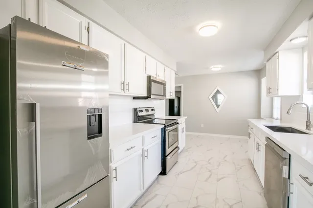 a kitchen with stainless steel appliances granite countertop a refrigerator a stove a sink and white cabinets with wooden floor