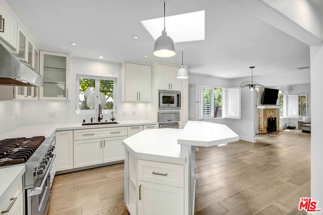 a kitchen with stainless steel appliances kitchen island granite countertop a stove a sink a refrigerator and white cabinets with wooden floor