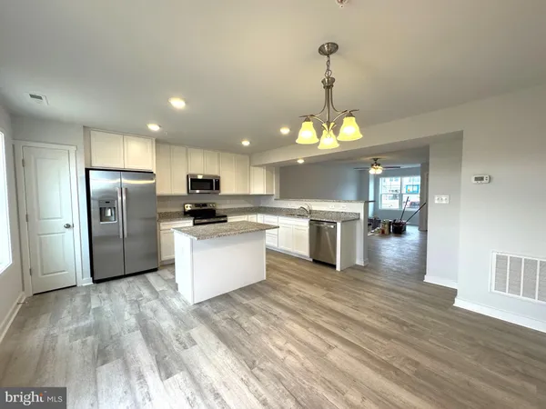 a kitchen with stainless steel appliances granite countertop a refrigerator a sink dishwasher a stove and white cabinets with wooden floor