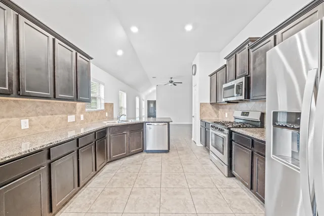 a large kitchen with stainless steel appliances granite countertop a stove top oven a sink dishwasher and a refrigerator