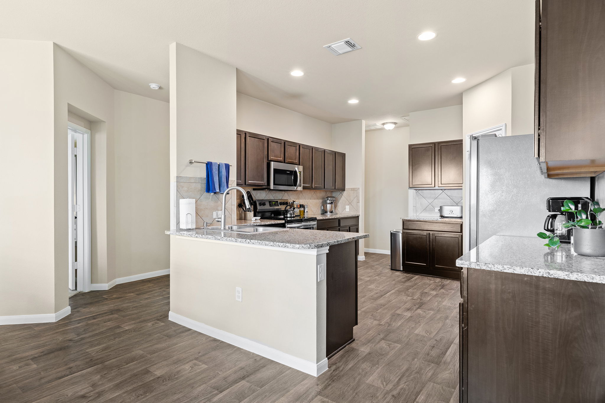 404 Cassandra Drive Hutto, TX 78634 - Photo 11 of 40 Kitchen with dark wood finish cabinetry, stainless steel appliances, light stone counters, and dark wood-type flooring