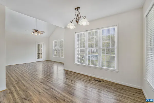an empty room with wooden floor chandelier fan and windows