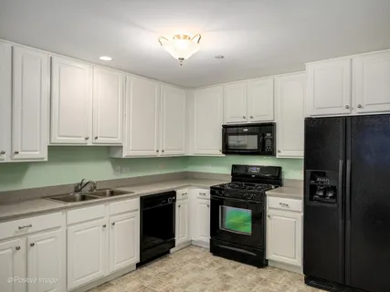 a kitchen with granite countertop white cabinets a refrigerator and a sink