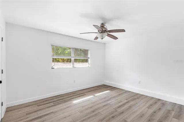 an empty room with wooden floor fan and windows