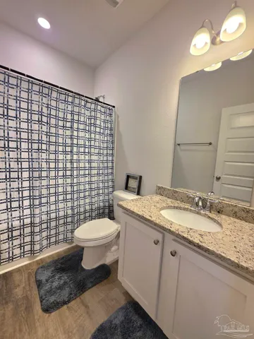 a bathroom with a granite countertop toilet a sink a mirror and shower curtain
