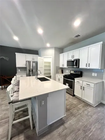 a large kitchen with kitchen island a stove a sink a refrigerator and white cabinets with wooden floor