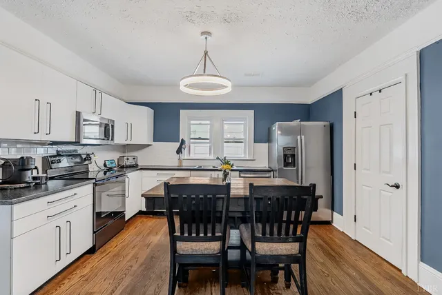 a kitchen with stainless steel appliances a dining table chairs refrigerator and cabinets