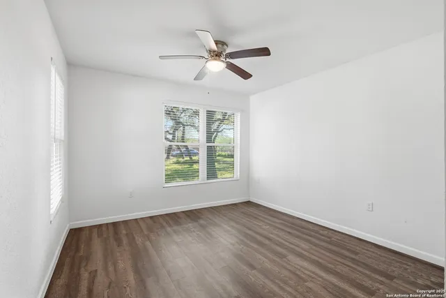 an empty room with wooden floor fan and windows