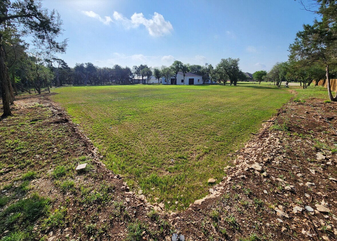 102 County Road 180 Leander, TX 78641 - Photo 18 of 25 An expansive green field offers a tranquil setting with distant structures nestled amongst a line of trees.