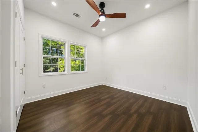 an empty room with wooden floor ceiling fan and windows