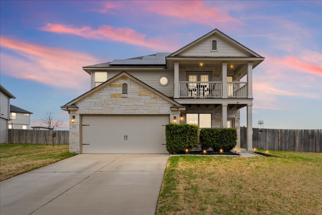 212 Plata Lane Jarrell, TX 76537 - Photo 5 of 30 View of front of house with roof mounted solar panels, stone siding, driveway, a garage, and a balcony
