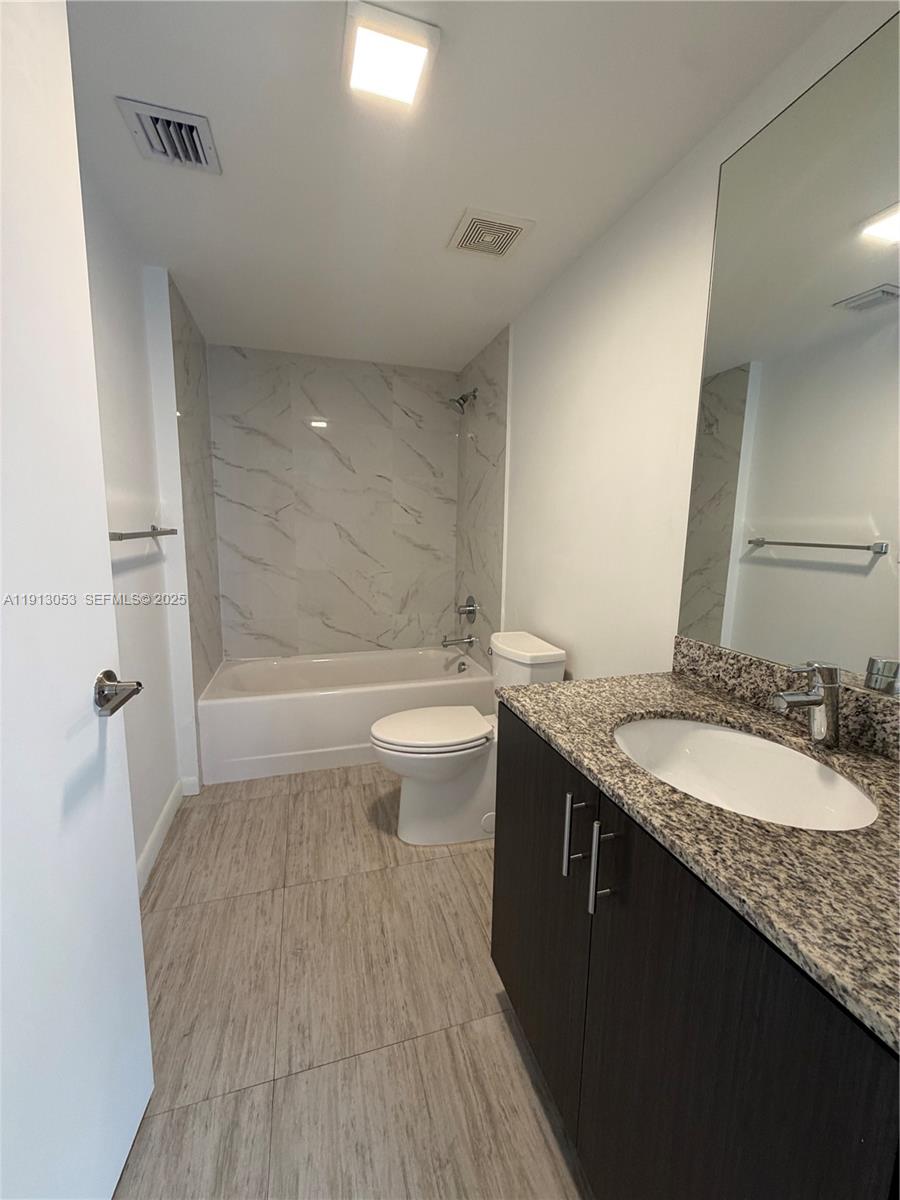 1801 Southwest 32nd Avenue, Unit 504 Miami, FL 33145 - Photo 13 of 14 a bathroom with a granite countertop sink a toilet a mirror and shower