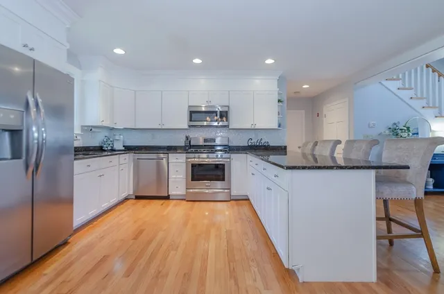 a large kitchen with stainless steel appliances granite countertop a stove a sink dishwasher a refrigerator and white cabinets with wooden floor