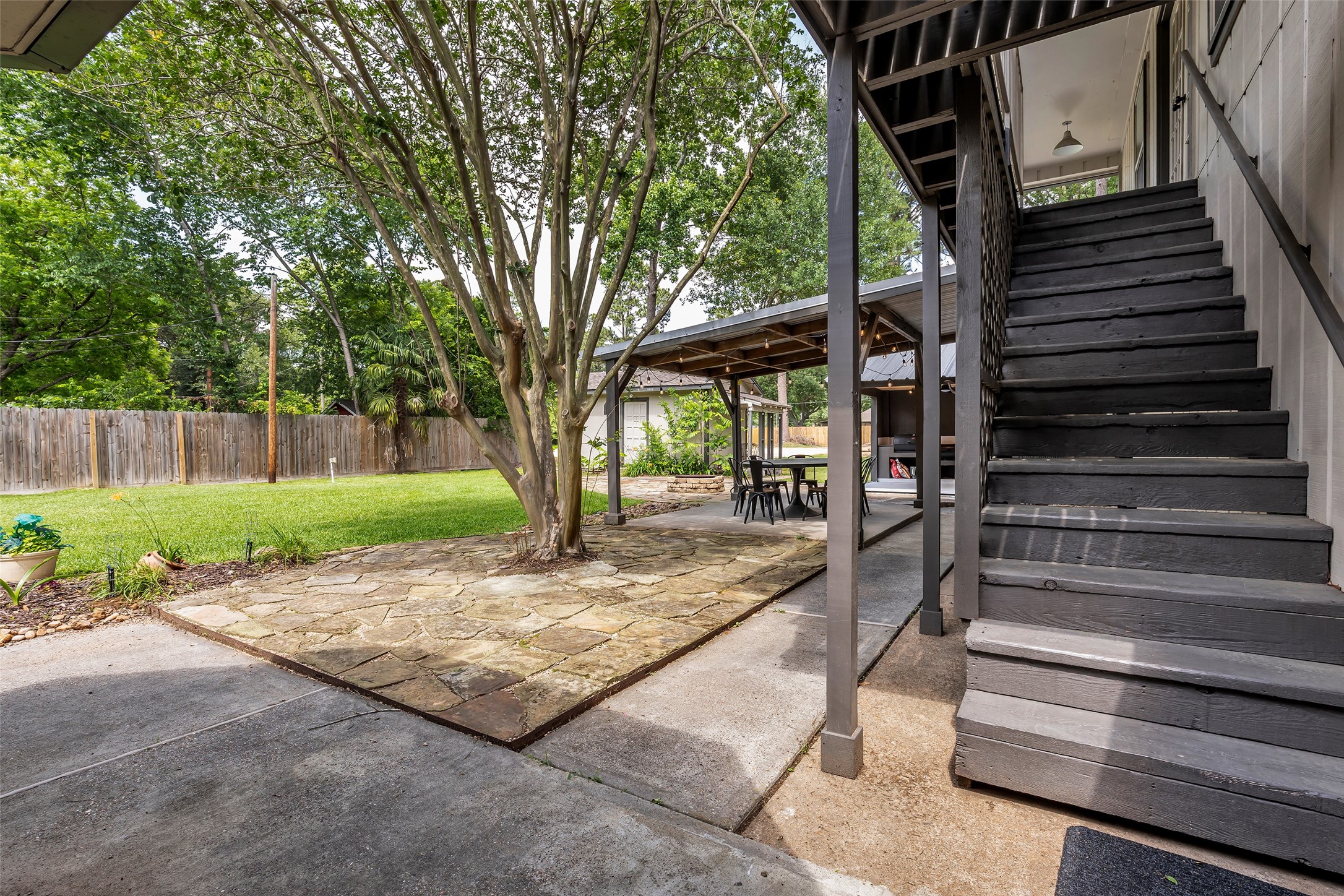22502 Fields Lane Spring, TX 77389 - Photo 24 of 39 Spacious backyard featuring a large tree, a stone patio, and a covered seating area. There's also a wooden staircase leading to an apartment, and the yard is bordered by a wooden fence, providing privacy and a serene atmosphere.