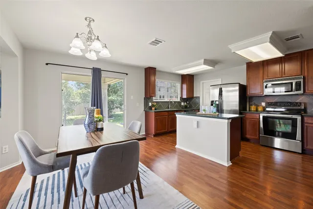 a kitchen with stainless steel appliances granite countertop a stove top oven a sink dishwasher a dining table and chairs with wooden floor