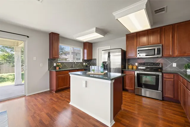 a kitchen with stainless steel appliances granite countertop a stove top oven a sink dishwasher a refrigerator and a microwave oven