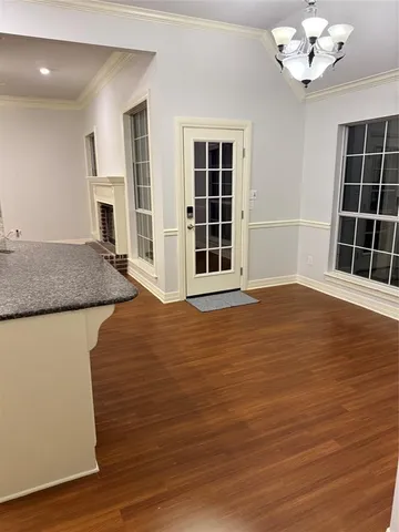 a view of an empty room with wooden floor and a kitchen
