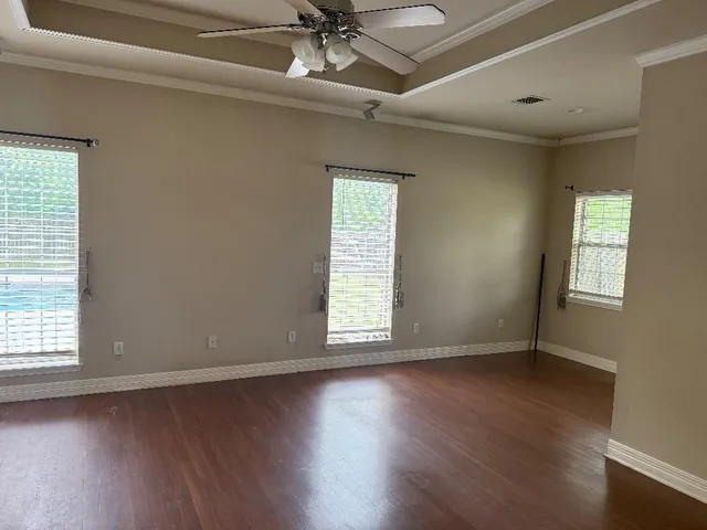 an empty room with wooden floor chandelier fan and windows