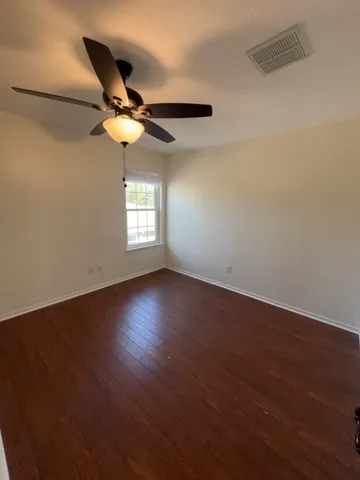 an empty room with wooden floor fan and windows