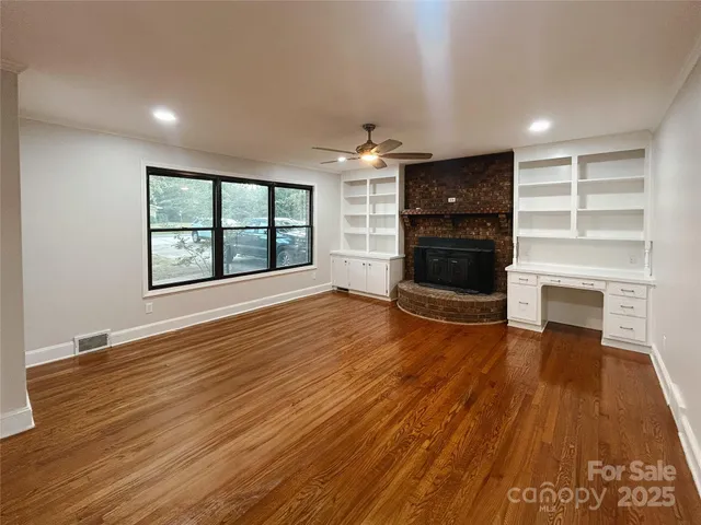 an empty room with wooden floor fireplace and windows