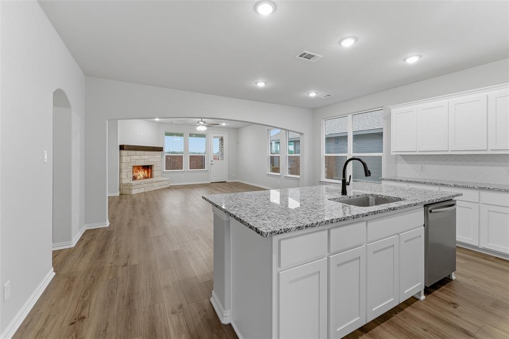 1329 Frio Drive Springtown, TX 76082 - Photo 7 of 25 Kitchen island featuring a stainless steel sink with a matte black faucet, granite countertops, white cabinetry, and wood-finish flooring