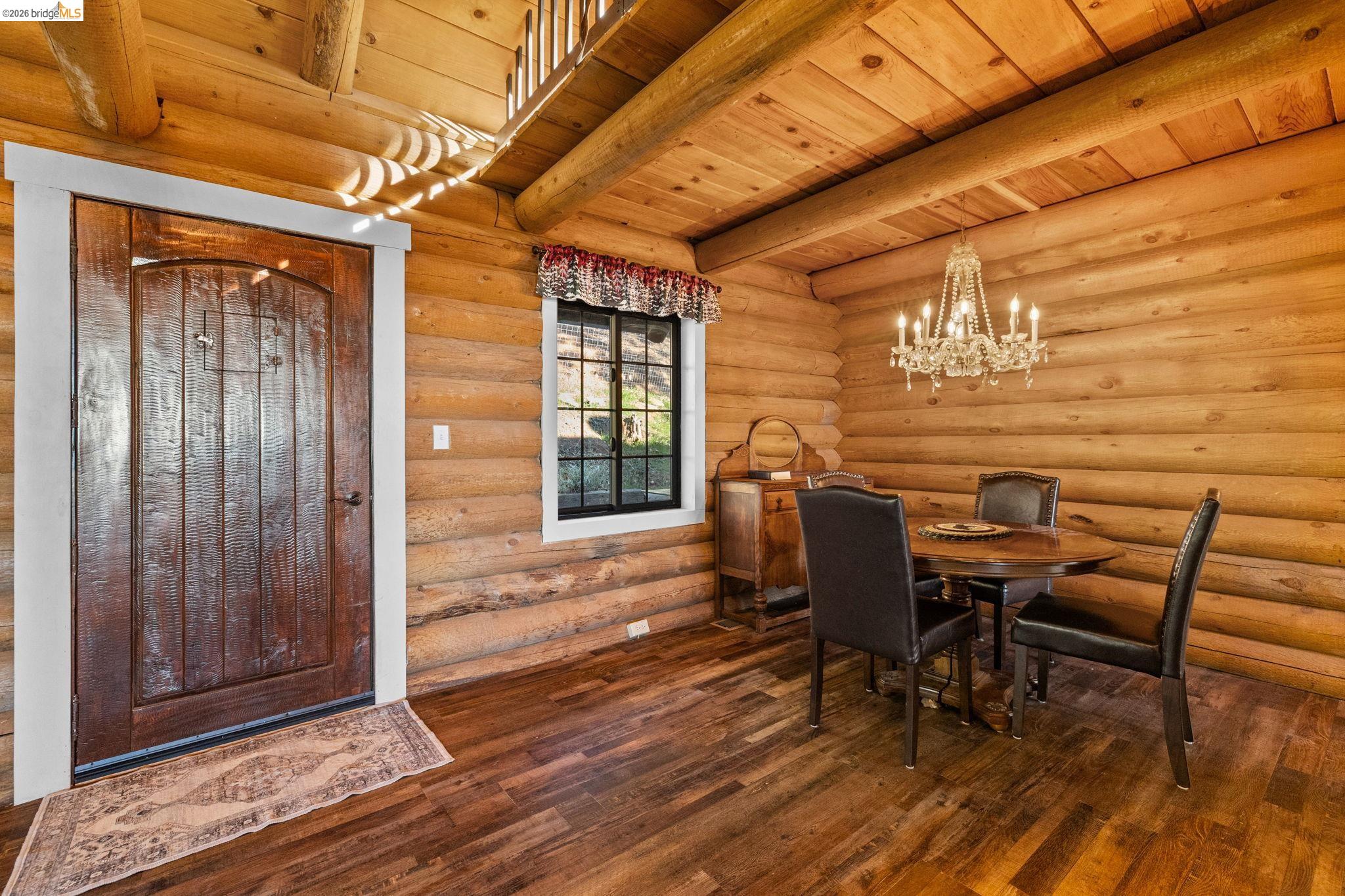 16144 Big Hill Road Sonora, CA 95370 - Photo 13 of 51 Log cabin interior featuring a prominent wooden entry door with white trim, wood-finish flooring, and exposed log walls