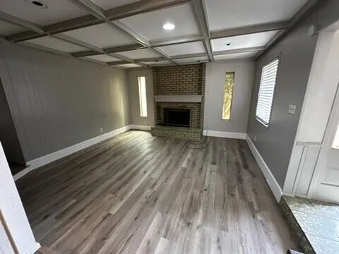 a view of an empty room with wooden floor fireplace and a window