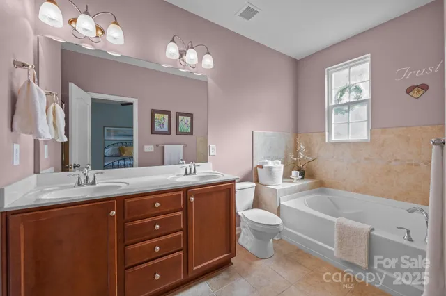 a spacious bathroom with a granite countertop double vanity sink a large mirror a toilet a bathtub and a window