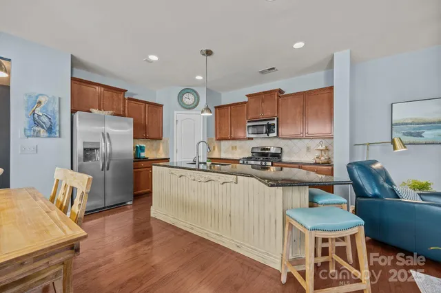 a kitchen with stainless steel appliances a refrigerator a stove a sink a dining table and chairs with wooden floor