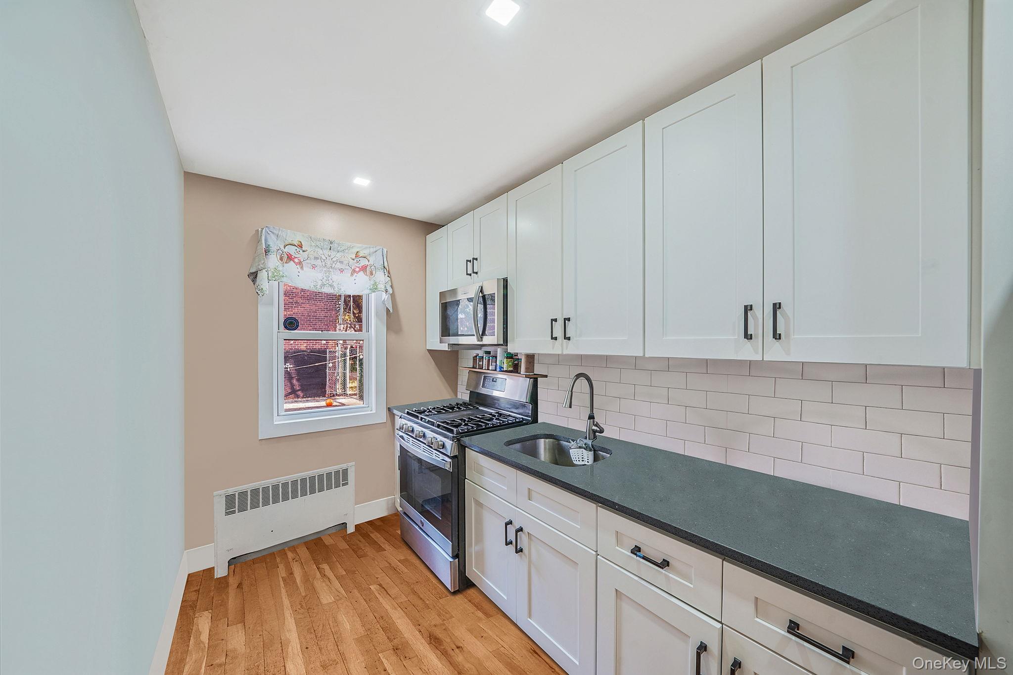 202-02 109th Avenue Queens, NY 11412 - Photo 11 of 26 Kitchen featuring stainless steel appliances, radiator heating unit, light wood-style floors, dark stone countertops, and recessed lighting