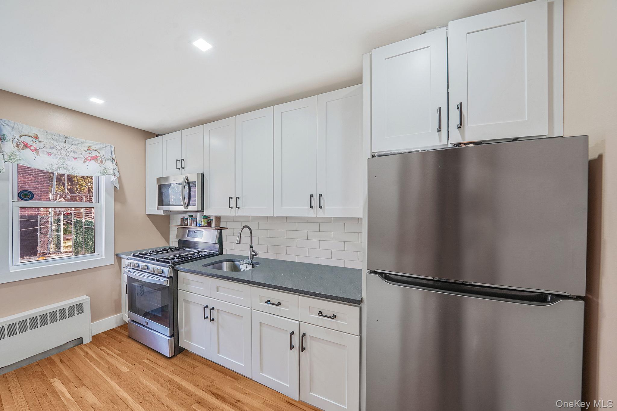 202-02 109th Avenue Queens, NY 11412 - Photo 12 of 26 Kitchen with stainless steel appliances, backsplash, white cabinets, light wood-style floors, and radiator heating unit