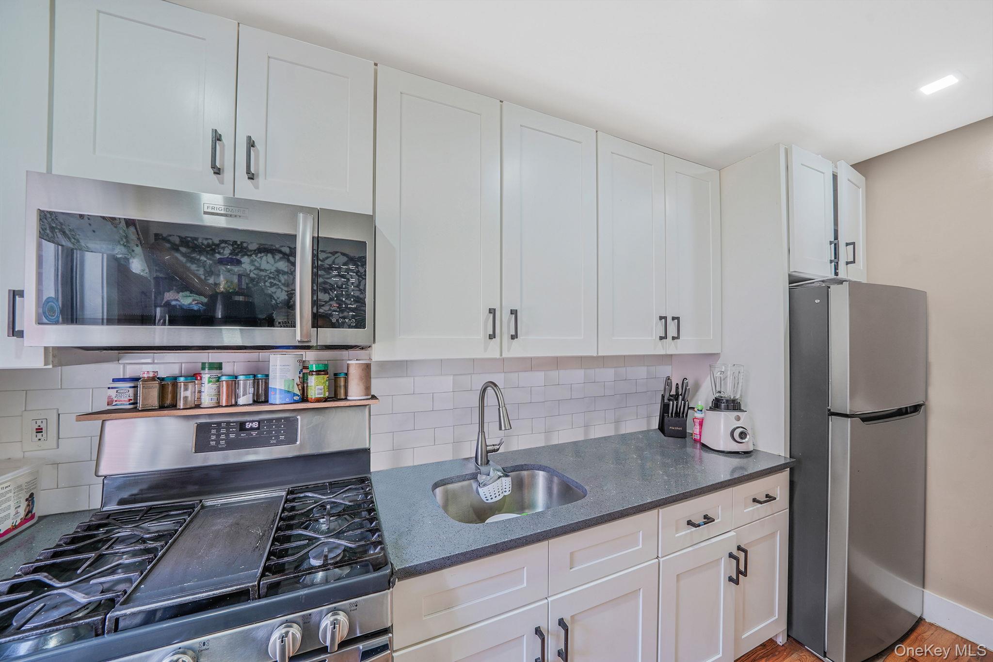 202-02 109th Avenue Queens, NY 11412 - Photo 14 of 26 Kitchen with appliances with stainless steel finishes, dark stone countertops, decorative backsplash, light wood-style flooring, and white cabinets
