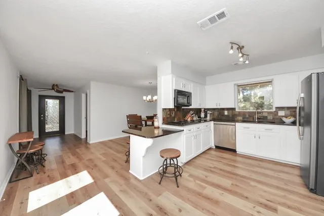 a large white kitchen with cabinets a sink dishwasher a stove and white countertops with wooden floor