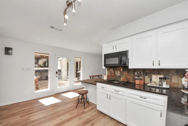 a kitchen with stainless steel appliances granite countertop a stove top oven a sink dishwasher a dining table and chairs with wooden floor