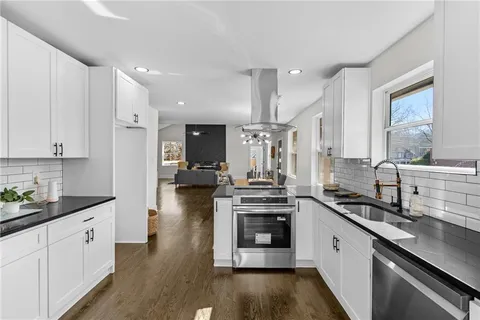a kitchen with stainless steel appliances kitchen island granite countertop a stove a sink and white cabinets