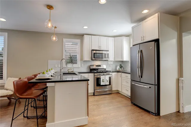 a kitchen with stainless steel appliances granite countertop a refrigerator a sink a stove a dining table and chairs