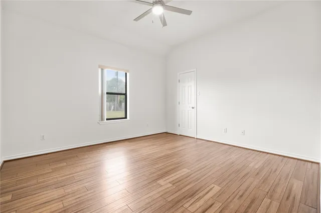 an empty room with wooden floor chandelier fan and windows