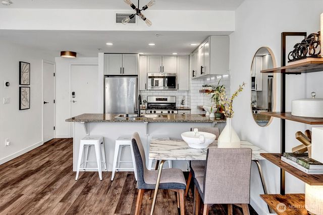 a kitchen with stainless steel appliances granite countertop a stove a refrigerator a kitchen island a dining table and chairs with wooden floor