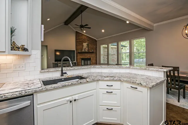a kitchen with granite countertop a sink stainless steel appliances white cabinets and a large window