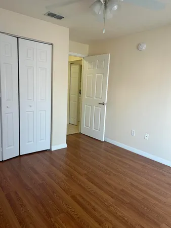 a view of an empty room with wooden floor and a ceiling fan