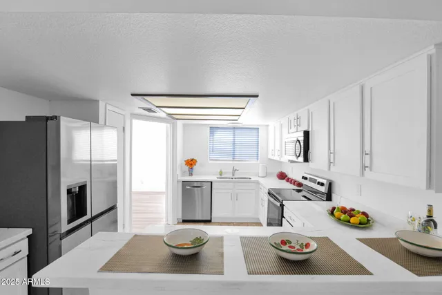 a kitchen with stainless steel appliances a sink a stove a refrigerator and white cabinets with wooden floor