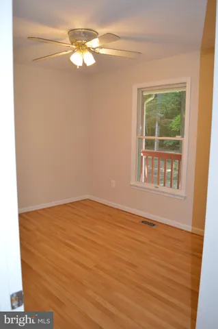 an empty room with wooden floor and way to kitchen