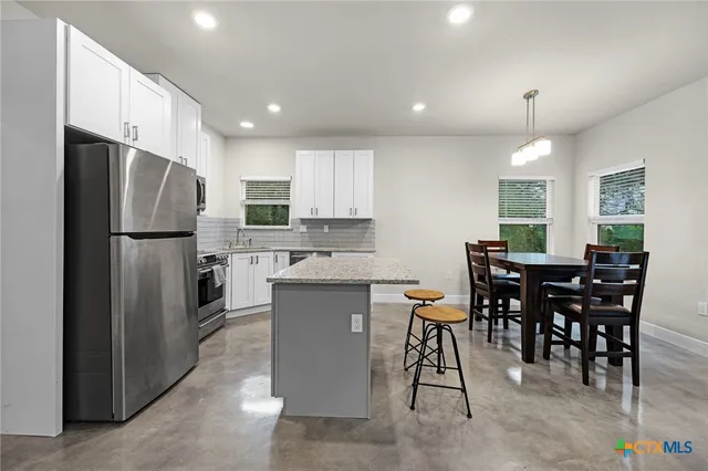 a kitchen with stainless steel appliances a dining table chairs refrigerator and cabinets