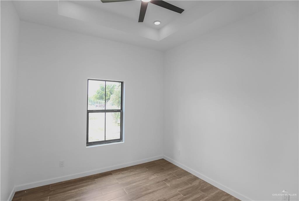 3730 East Davis Road Edinburg, TX 78542 - Photo 15 of 23 Unfurnished room with a tray ceiling, wood finished floors, baseboards, a ceiling fan, and recessed lighting