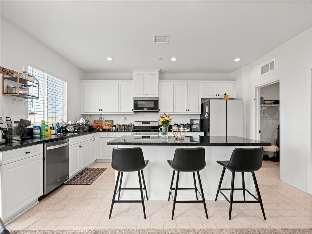 11520 Ferro Street Victorville, CA 92392 - Photo 8 of 40 a kitchen with stainless steel appliances kitchen island a table chairs in it and white cabinets