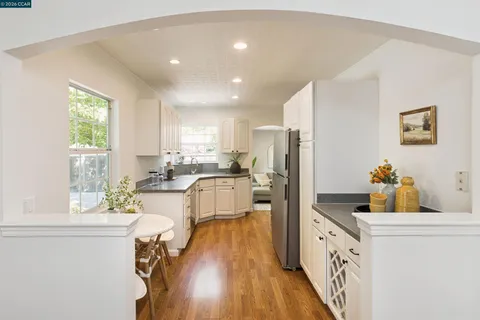 a kitchen with granite countertop a refrigerator a sink a stove and white cabinets with wooden floor