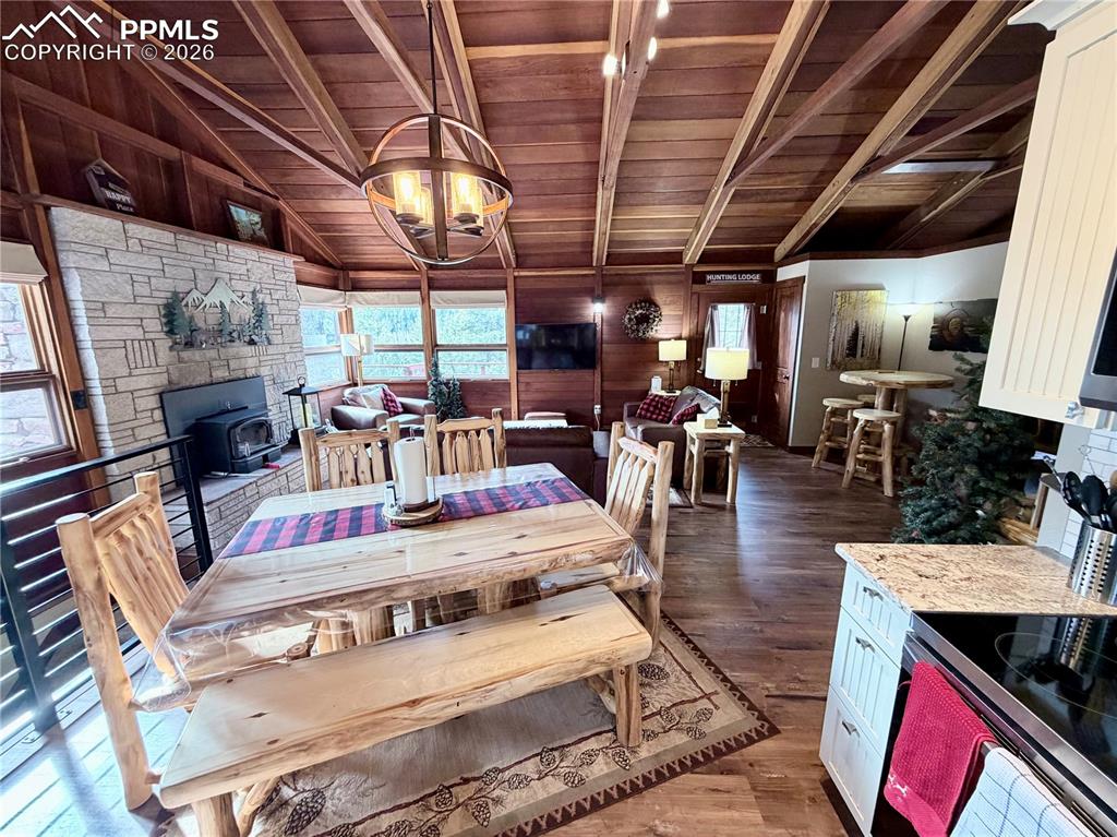 121 St Charles Drive Rye, CO 81069 - Photo 5 of 22 Dining space featuring dark wood finished floors, a wood stove, wood walls, plenty of natural light, and a chandelier