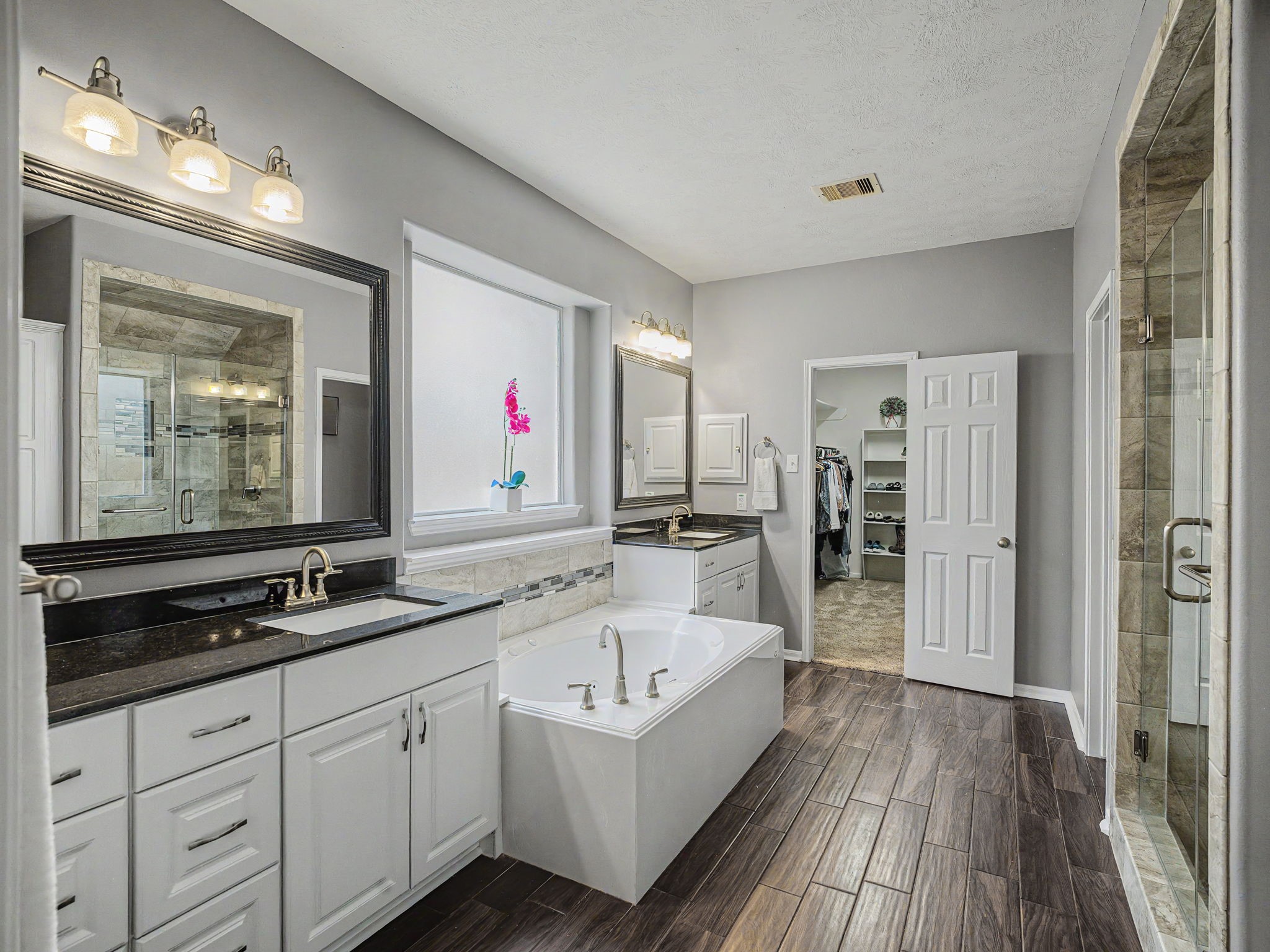 2210 Fox Path Katy, TX 77494 - Photo 27 of 47 Featuring ultimate convenience, the space boasts two separate white vanities topped with sleek black granite counters, under-mount sinks, and ornate dark-framed mirrors. Nestled perfectly between them is a large whirlpool soaking tub anchored by a frosted-glass privacy window that welcomes in bright natural light.
