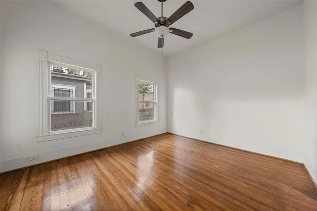 an empty room with wooden floor chandelier fan and windows